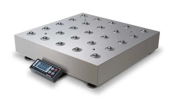 A metallic roller conveyor scale, designed for precise weighing solutions, features multiple small, round rollers embedded on its surface. Attached to the side is a digital control panel with display and buttons. The scale rests on four sturdy feet, ideal for rigorous industrial scales inspection.